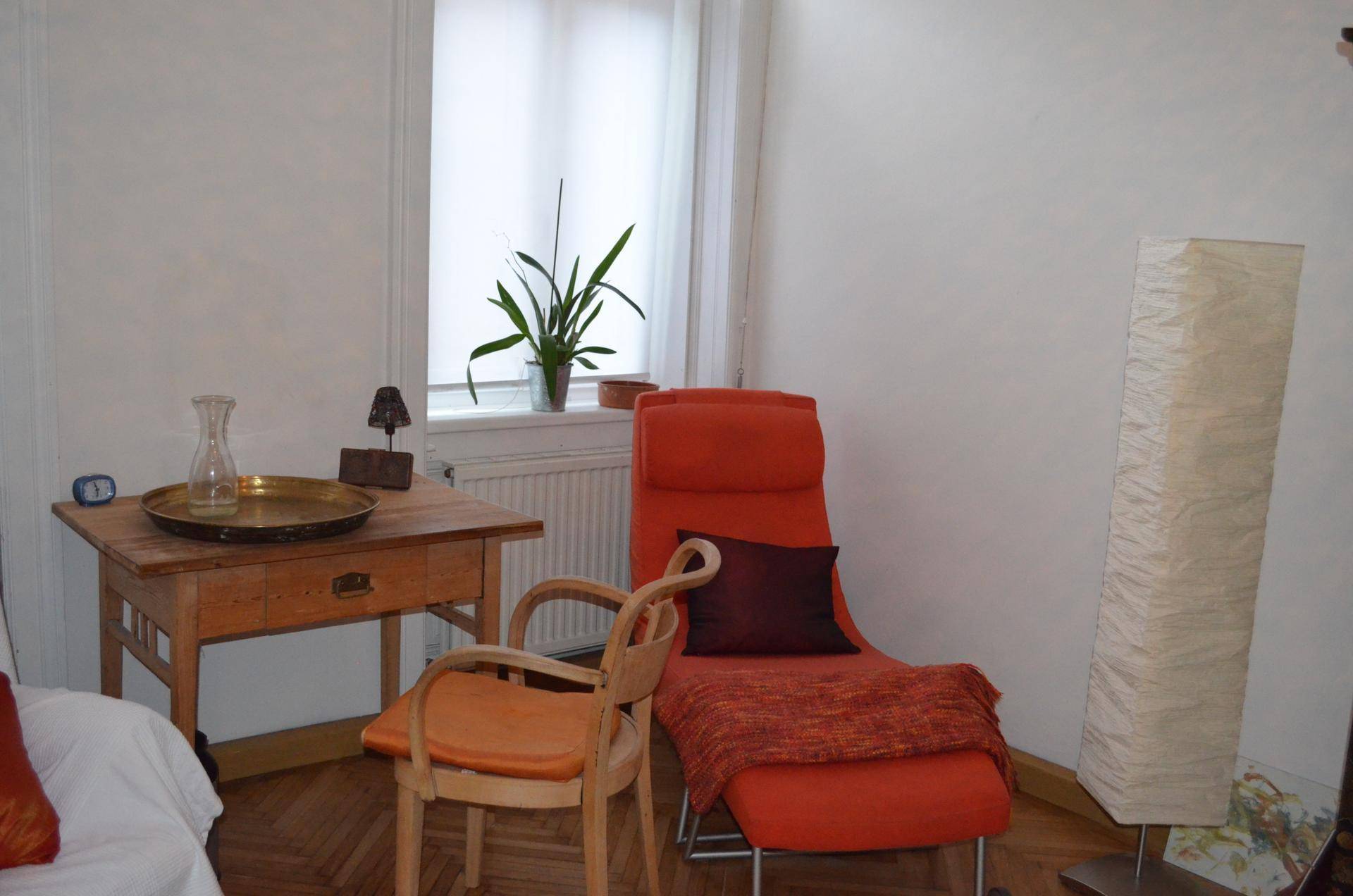 Gemütlicher Bereich mit einem Holztisch, einer orangefarbenen Liege und einem Fenster, das für natürliches Licht sorgt.