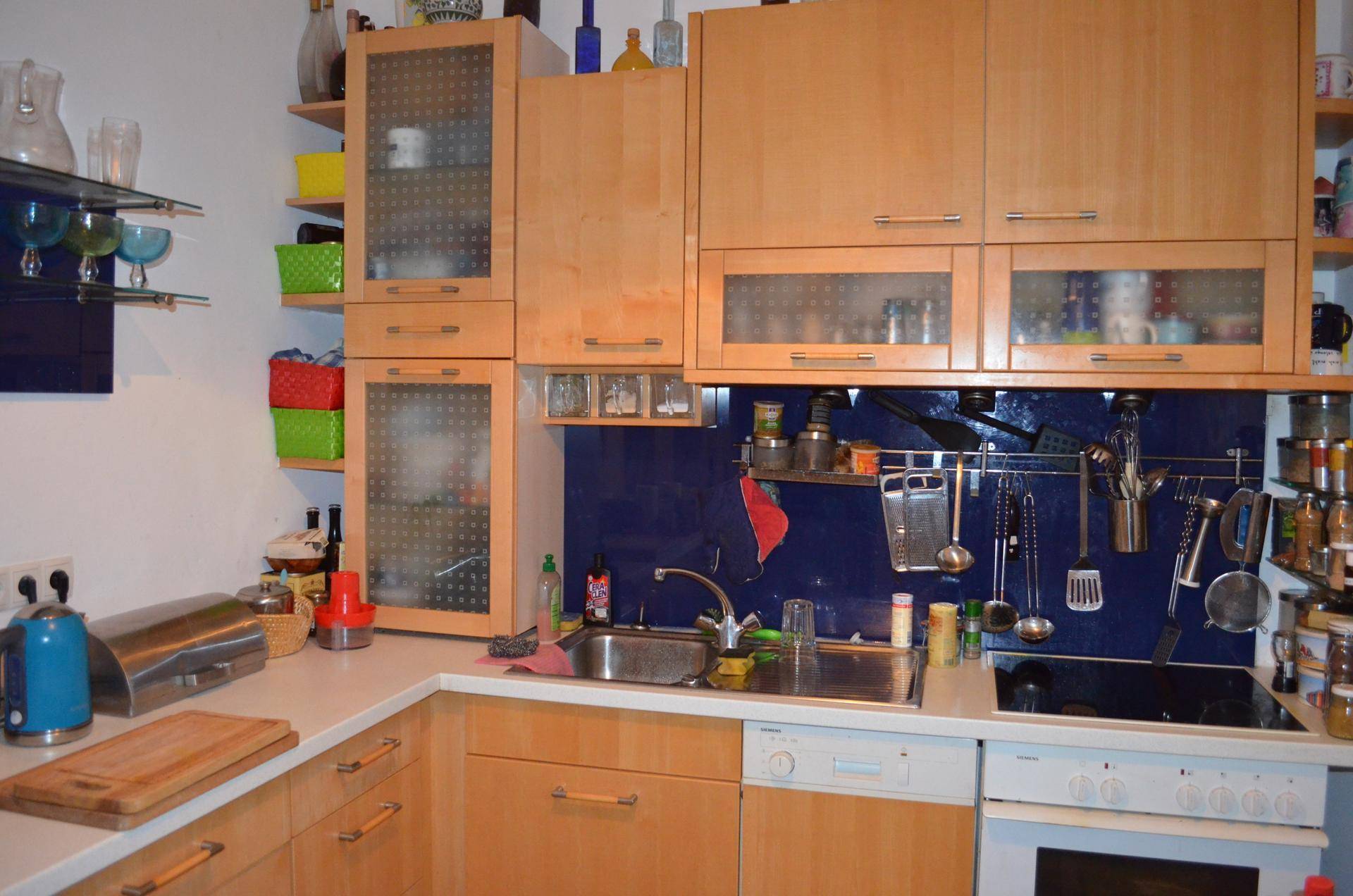 Funktionale Küche mit hellen Holzschränken, einer blauen Rückwand und integrierten Haushaltsgeräten für den täglichen Gebrauch.