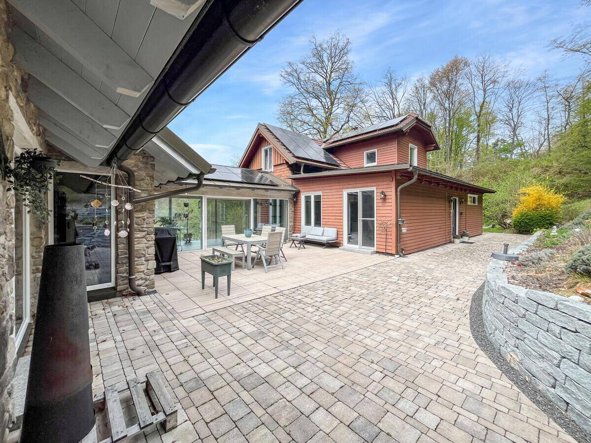 Gepflasterte Terrasse mit Steinfassade und Blick auf die grüne Umgebung.