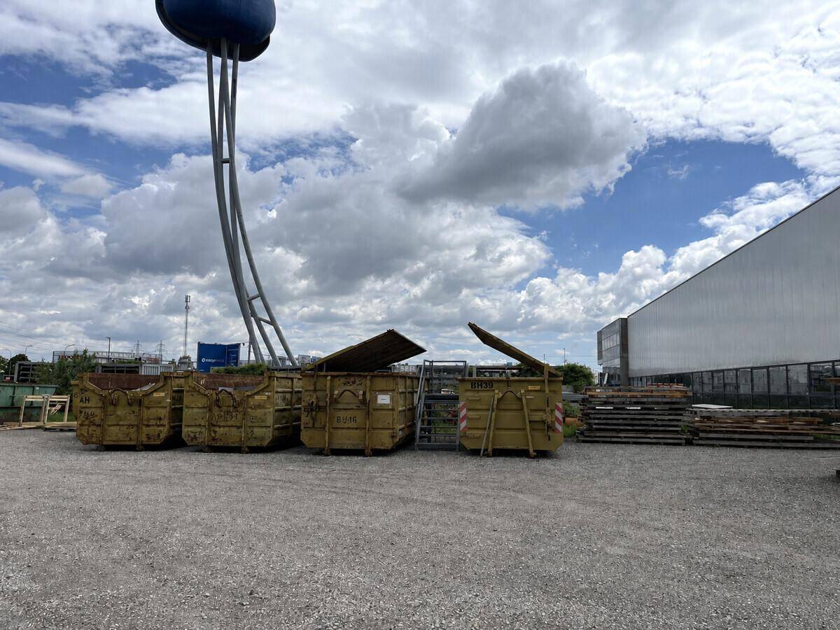 Außenbereich eines Industriegeländes mit Containern, Lagerflächen und einem Wasserturm unter blauem Himmel.