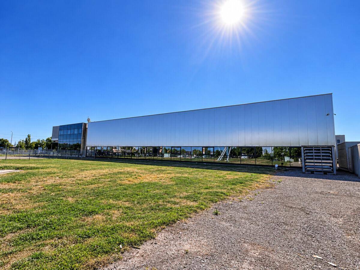 Lange Ansicht eines modernen Industriegebäudes mit reflektierender Fassade und Grünfläche im Vordergrund.