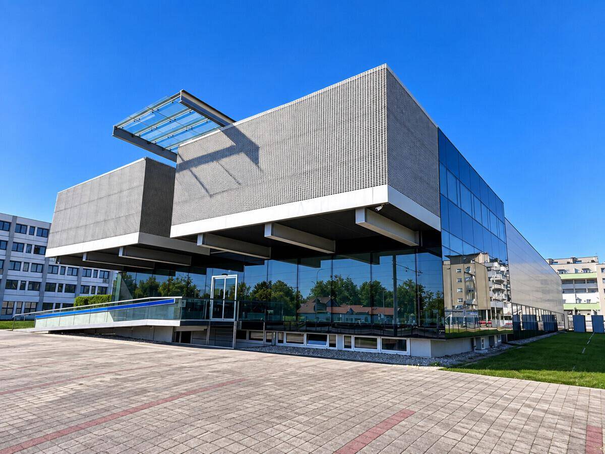 Seitliche Ansicht des modernen Bürokomplexes mit Glasfassade und klarem Himmel, umgeben von Pflastersteinen.