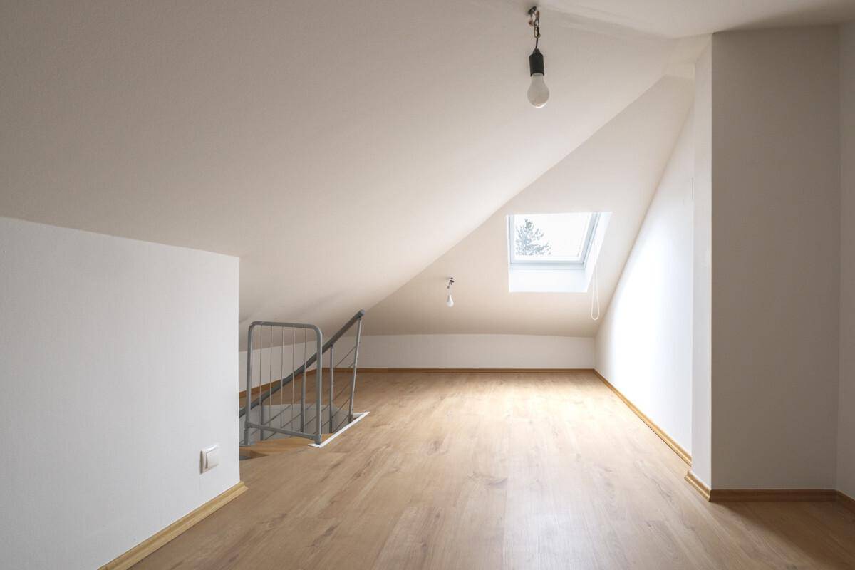 Helles Dachzimmer mit Holzplankenboden, Dachfenster und Geländer für den Treppenabgang.