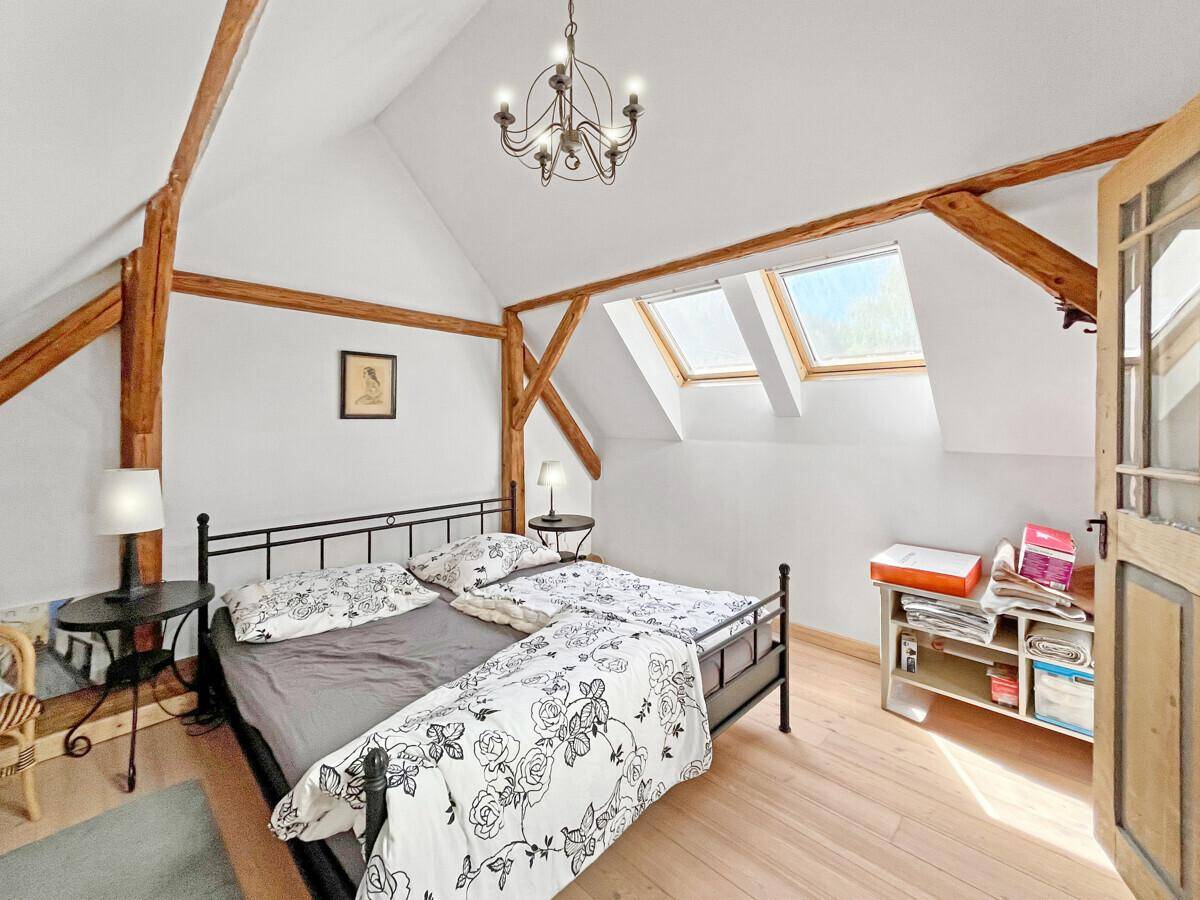 Helles Schlafzimmer im Dachgeschoss mit Holzbalken, Dachfenstern und einfacher Einrichtung.