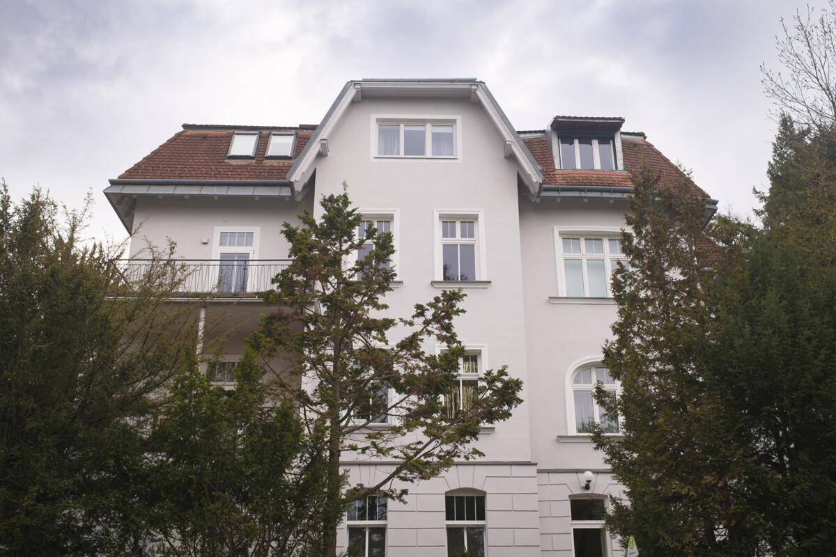 Elegante Fassade eines großen Gebäudes mit hellen Wänden, vielen Fenstern und einem roten Ziegeldach.