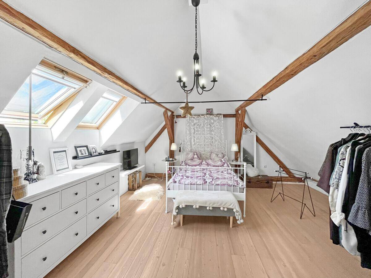 Geräumiges Schlafzimmer im Dachgeschoss mit Holzbalken, Dachfenstern und weißer Kommode.