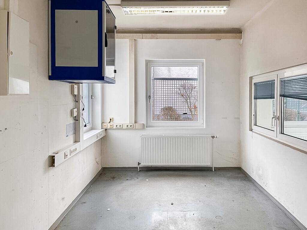 Kleiner Büroraum mit Fenster, Heizkörper und Wandinstallationen, ideal für administrative Aufgaben.