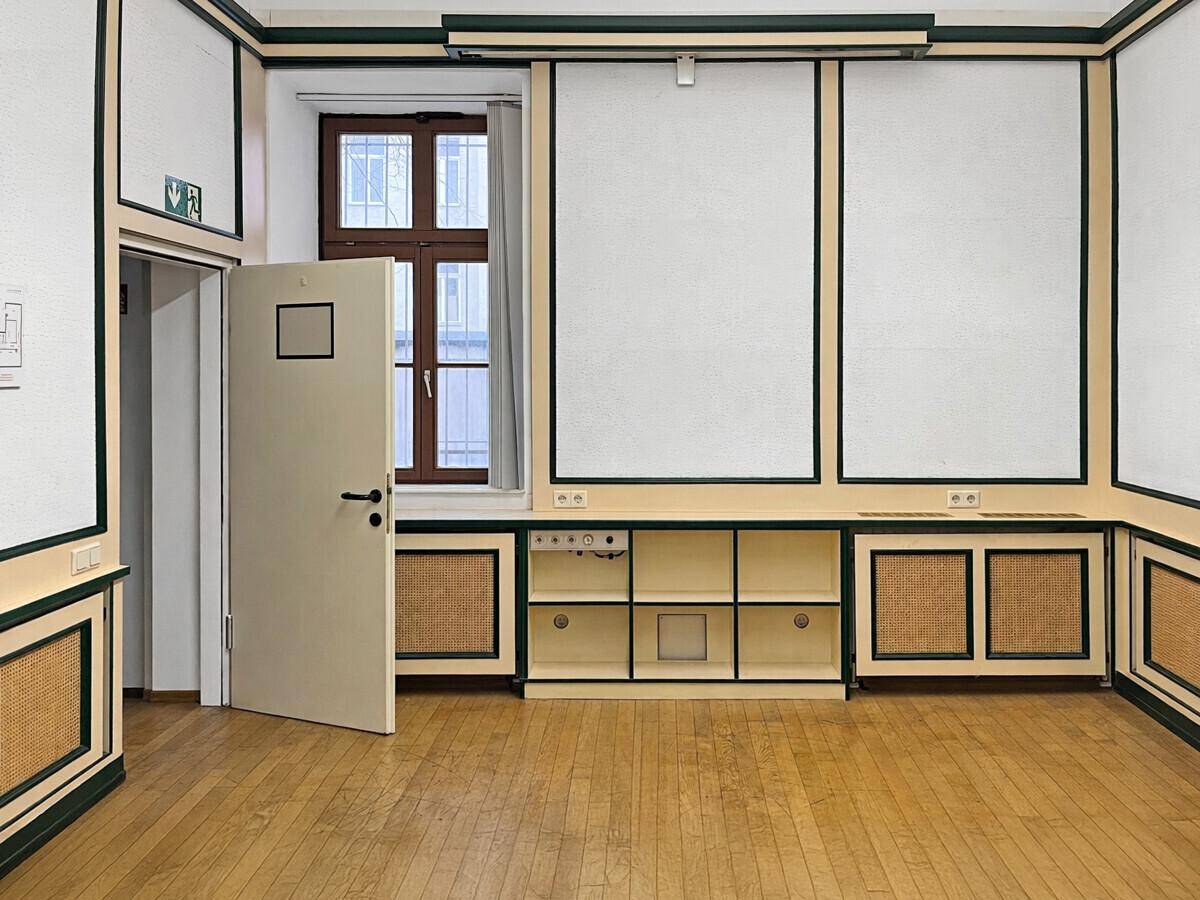 Büroraum mit Holzboden, dekorativen Wandpaneelen, integrierten Regalen und einem Fenster mit Blick nach draußen.