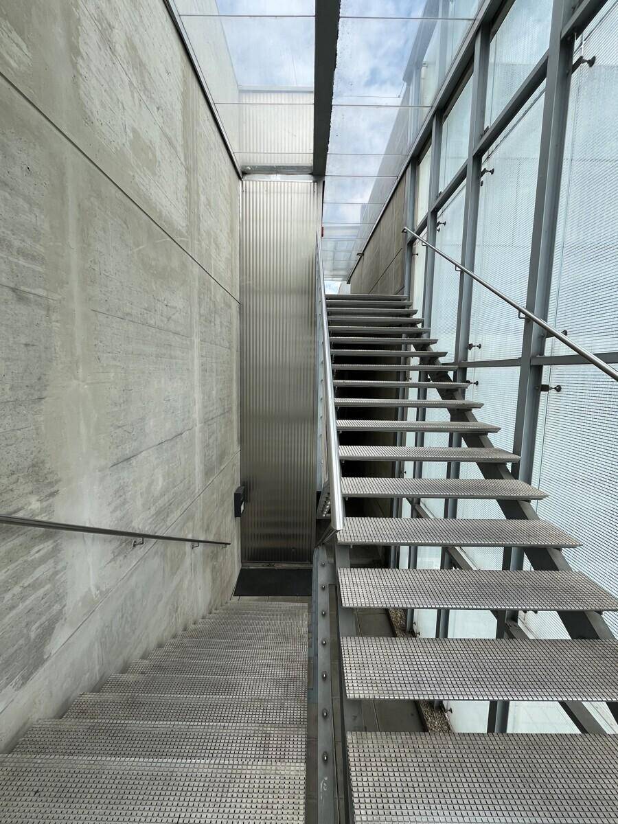 Industrielle Metalltreppe mit Glaswänden und Oberlicht, die mehrere Etagen in einem modernen Gebäude verbindet.