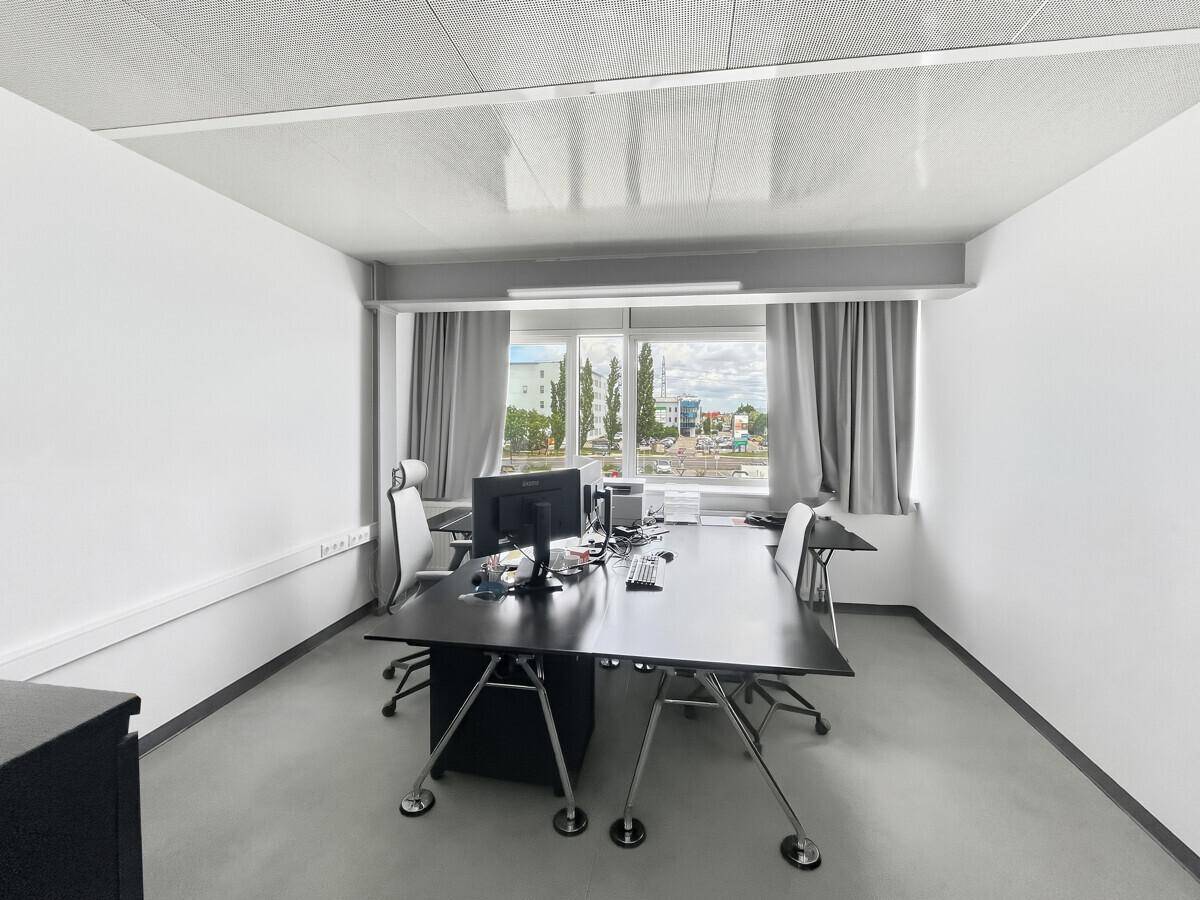 Helles Einzelbüro mit modernem Schreibtisch, Bürostühlen und Blick nach draußen durch ein großes Fenster.