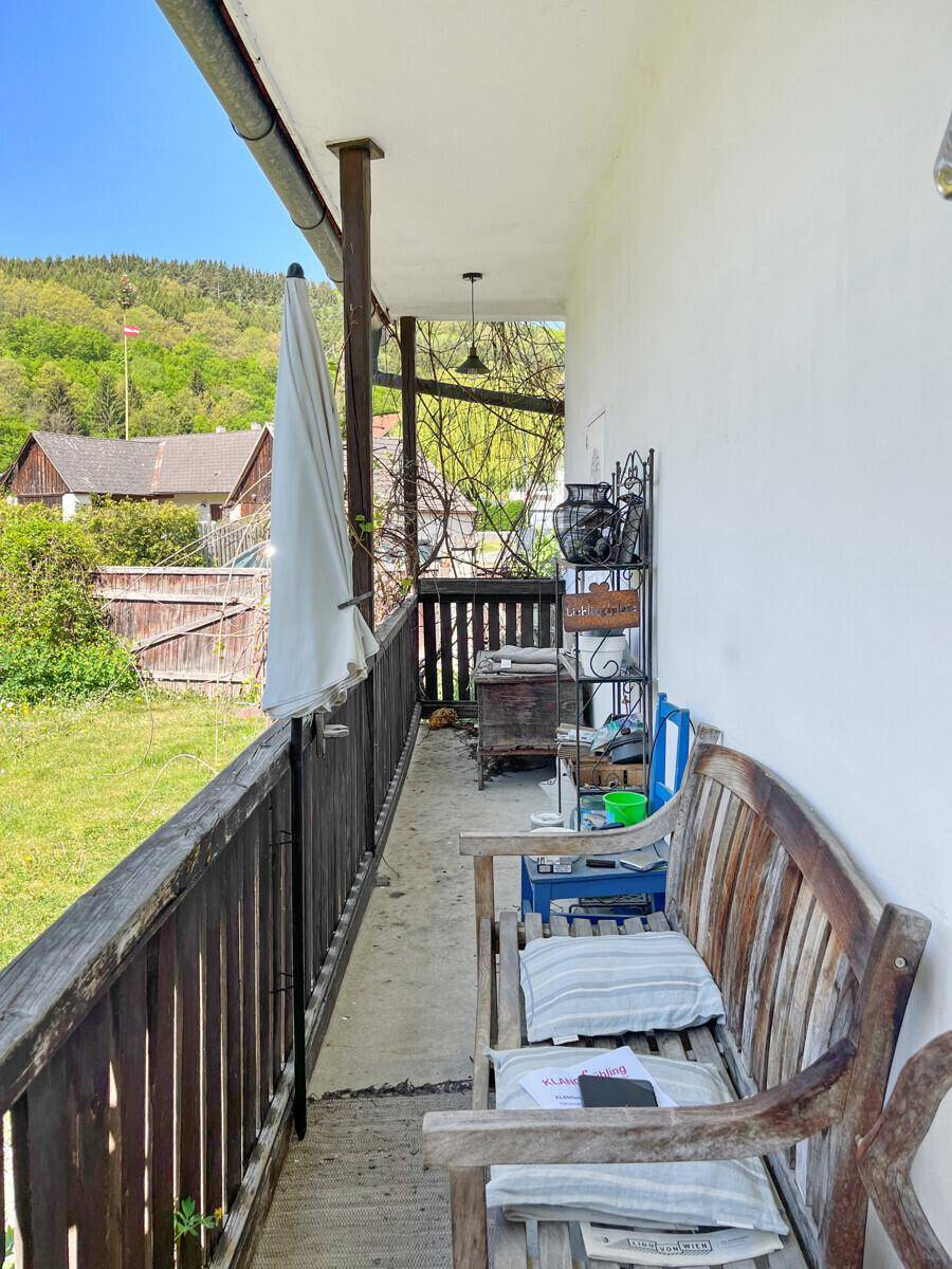Langer, überdachter Balkon mit Holzboden und Blick ins Grüne.