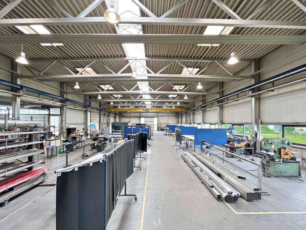 Große, helle Lagerhalle mit hohen Decken, Oberlichtern und industrieller Ausstattung für Produktion.