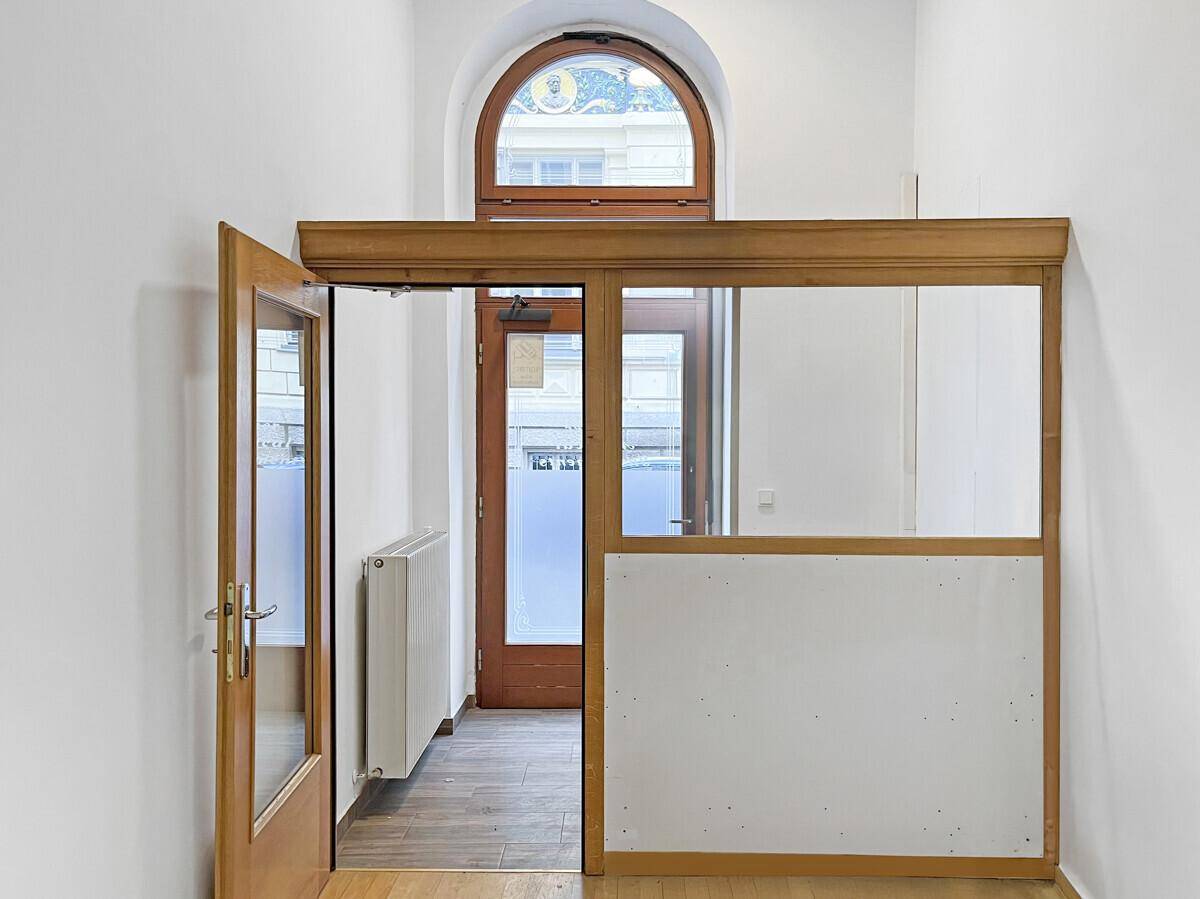 Eingangsbereich mit Holztür, Glasabtrennung, Heizkörper und einem dekorativen Bogenfenster oben.