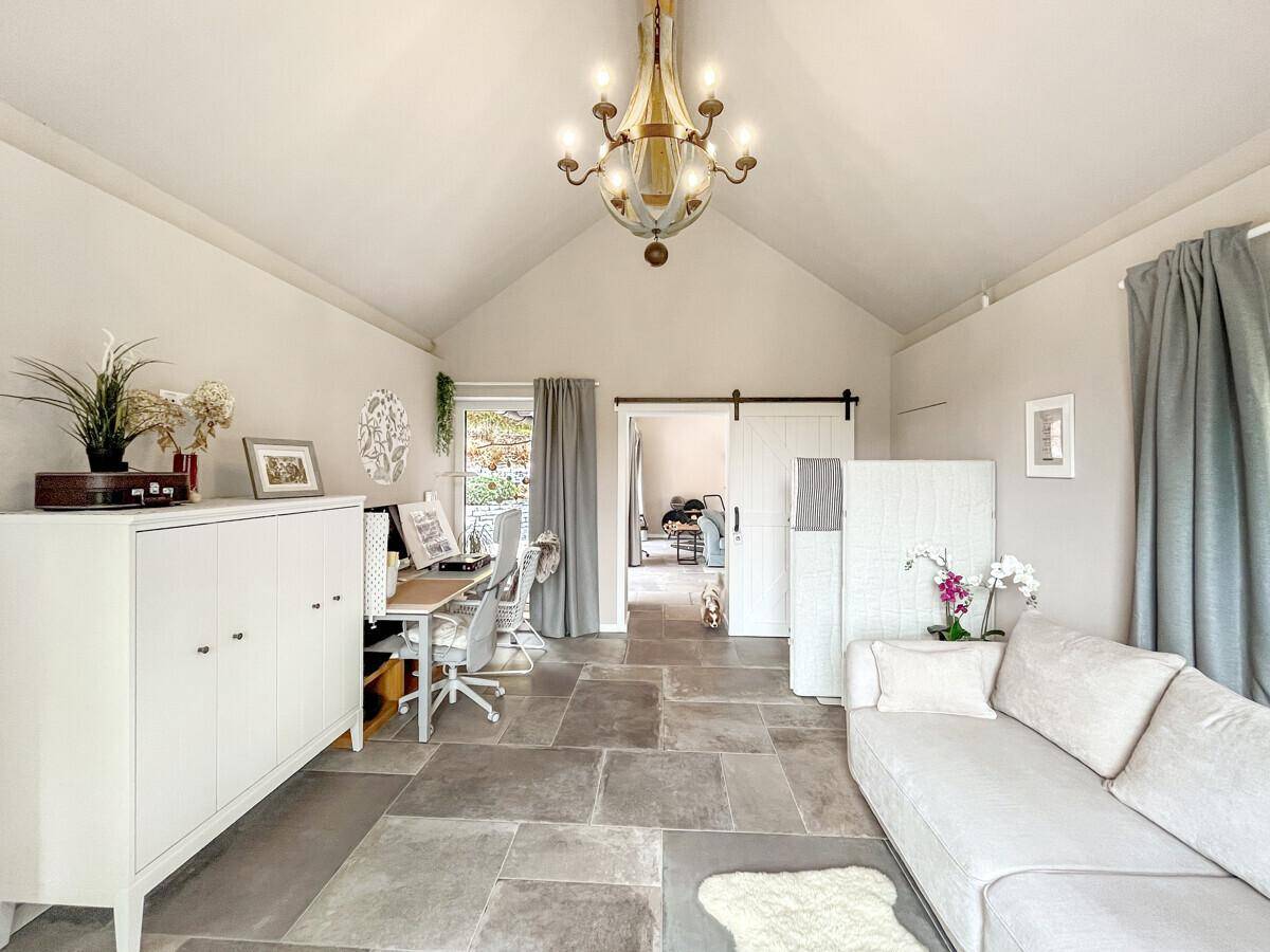 Geräumiges Wohnzimmer mit hohen Decken, Steinfliesen und Schiebetür.