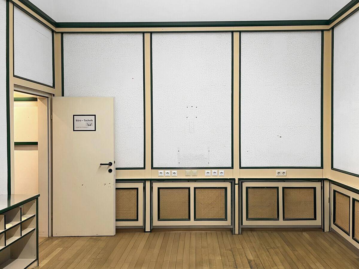 Heller Büroraum mit Holzboden, strukturierten Wandpaneelen und integrierten Ablageflächen, bereit zur Nutzung.