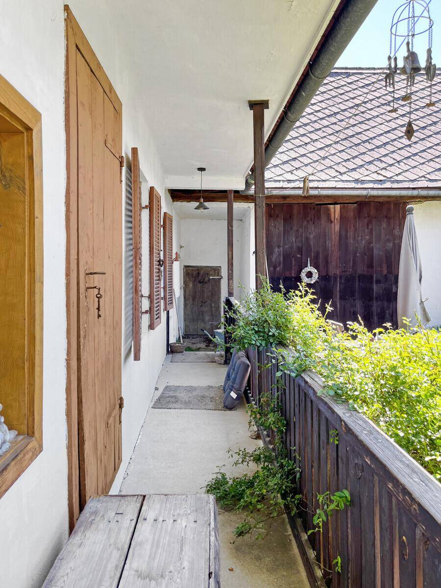 Überdachter Balkon mit Holzboden, Fensterläden und Blick auf den Innenhof.