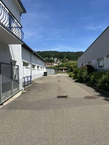 Zufahrtsweg zwischen zwei Gewerbegebäuden mit Blick auf die umliegende grüne Hügellandschaft.