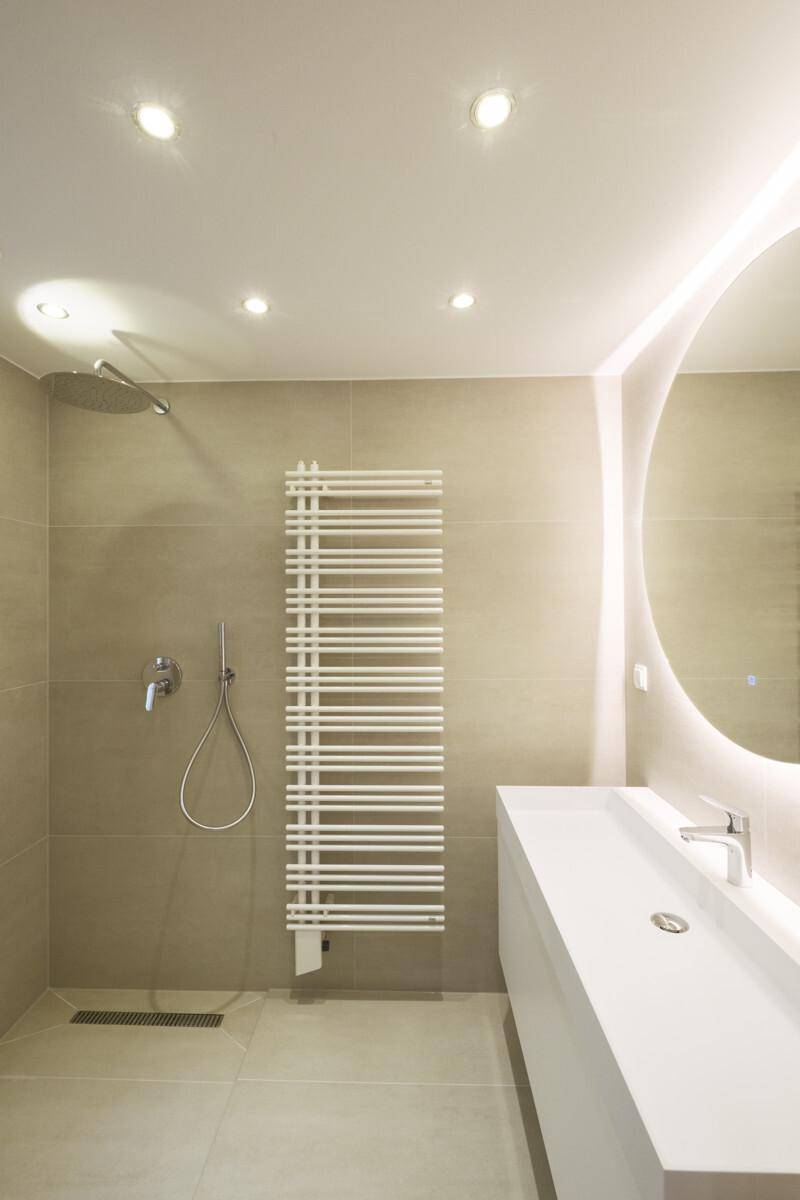 Modernes Badezimmer mit Regendusche, beleuchtetem Spiegel, schwebendem Waschtisch und Handtuchheizkörper.