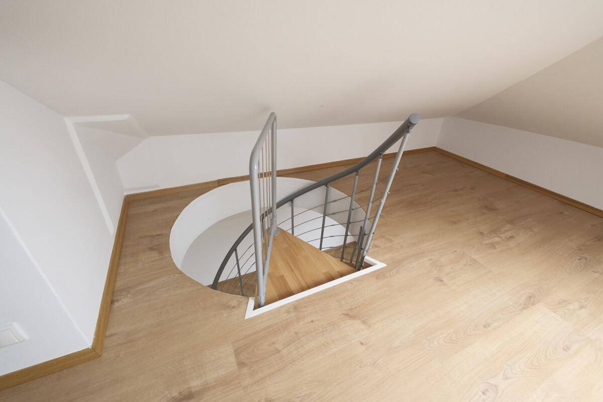 Blick von einem Dachzimmer auf den Abgang einer Wendeltreppe mit Holzplankenboden.