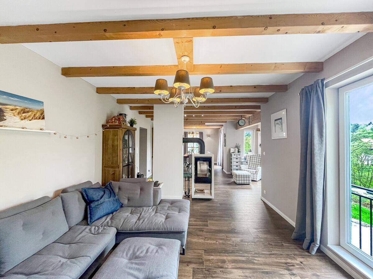 Helles Wohnzimmer mit Holzbalkendecke, Sofa und Blick ins Grüne.