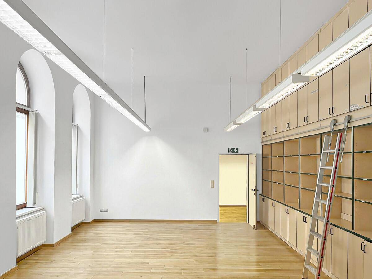 Geräumiger Büroraum mit hohen Decken, Holzboden, Bogenfenstern und integrierten Holzschränken mit Leiter.