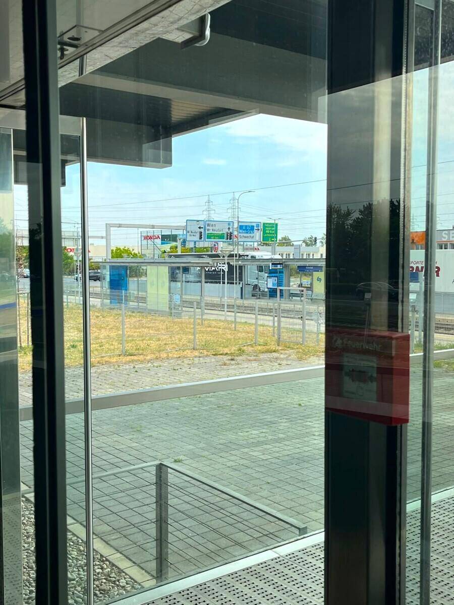 Blick durch eine Glasfassade auf eine Straße und eine Bushaltestelle mit Verkehrsschildern.