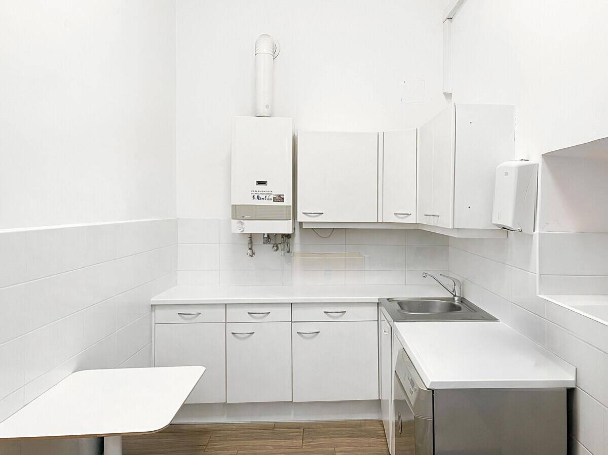 Kleine, funktionale Küchenzeile mit weißen Schränken, Spüle und einem Warmwasserbereiter an der Wand.