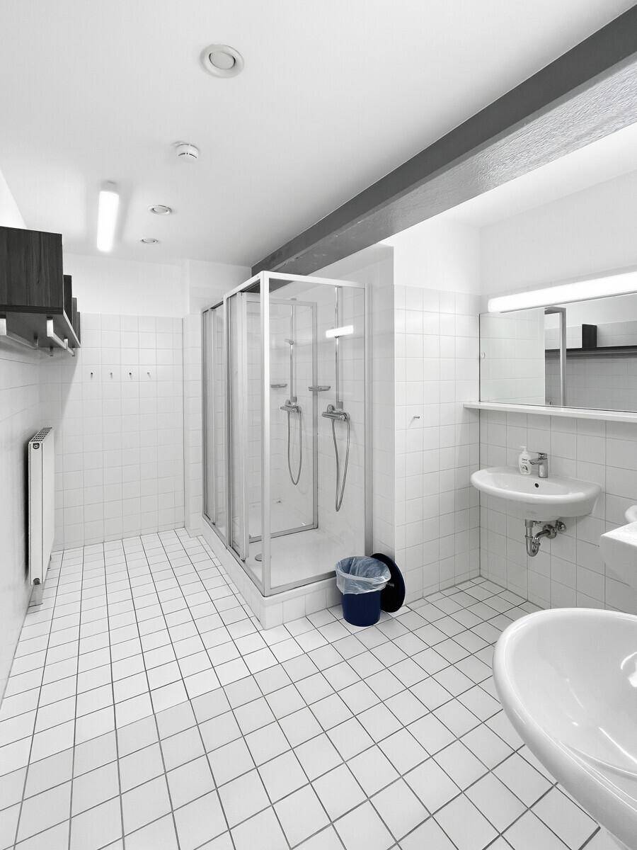 Helles Badezimmer mit Duschkabine, zwei Waschbecken und weißen Fliesen, sauber und funktional.