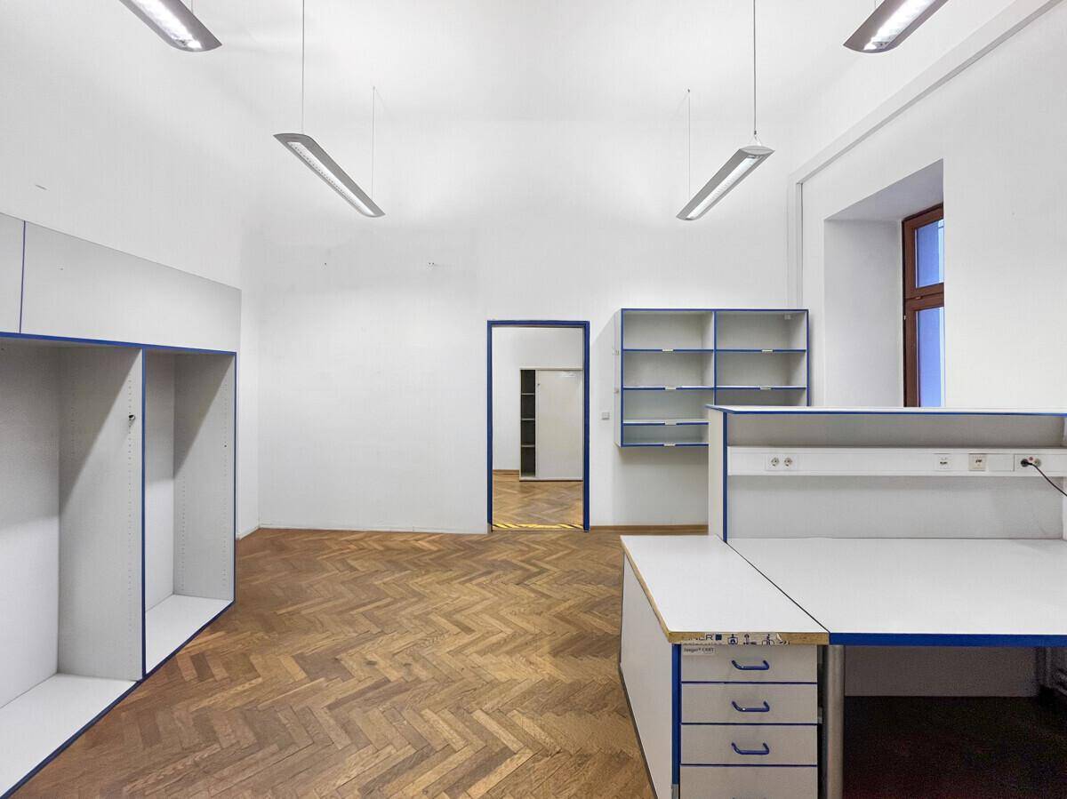 Blick in den Labor- oder Werkstattraum mit Fischgrätparkett, Arbeitsflächen und einem offenen Durchgang.