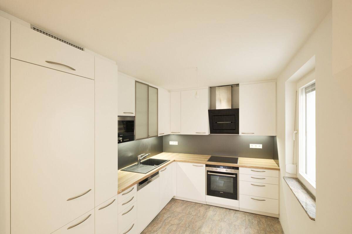 Moderne Einbauküche mit weißen Schränken, Holz-Arbeitsplatten und integrierten Geräten.