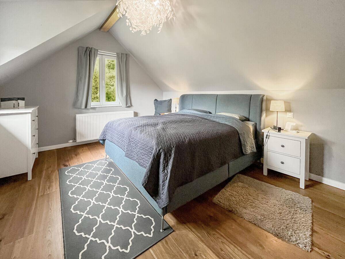 Helles Schlafzimmer im Dachgeschoss mit Holzboden, gemütlichem Bett und schräger Decke.