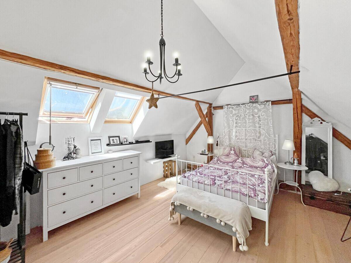 Helles Schlafzimmer im Dachgeschoss mit Holzbalken, Dachfenstern und minimalistischer Einrichtung.