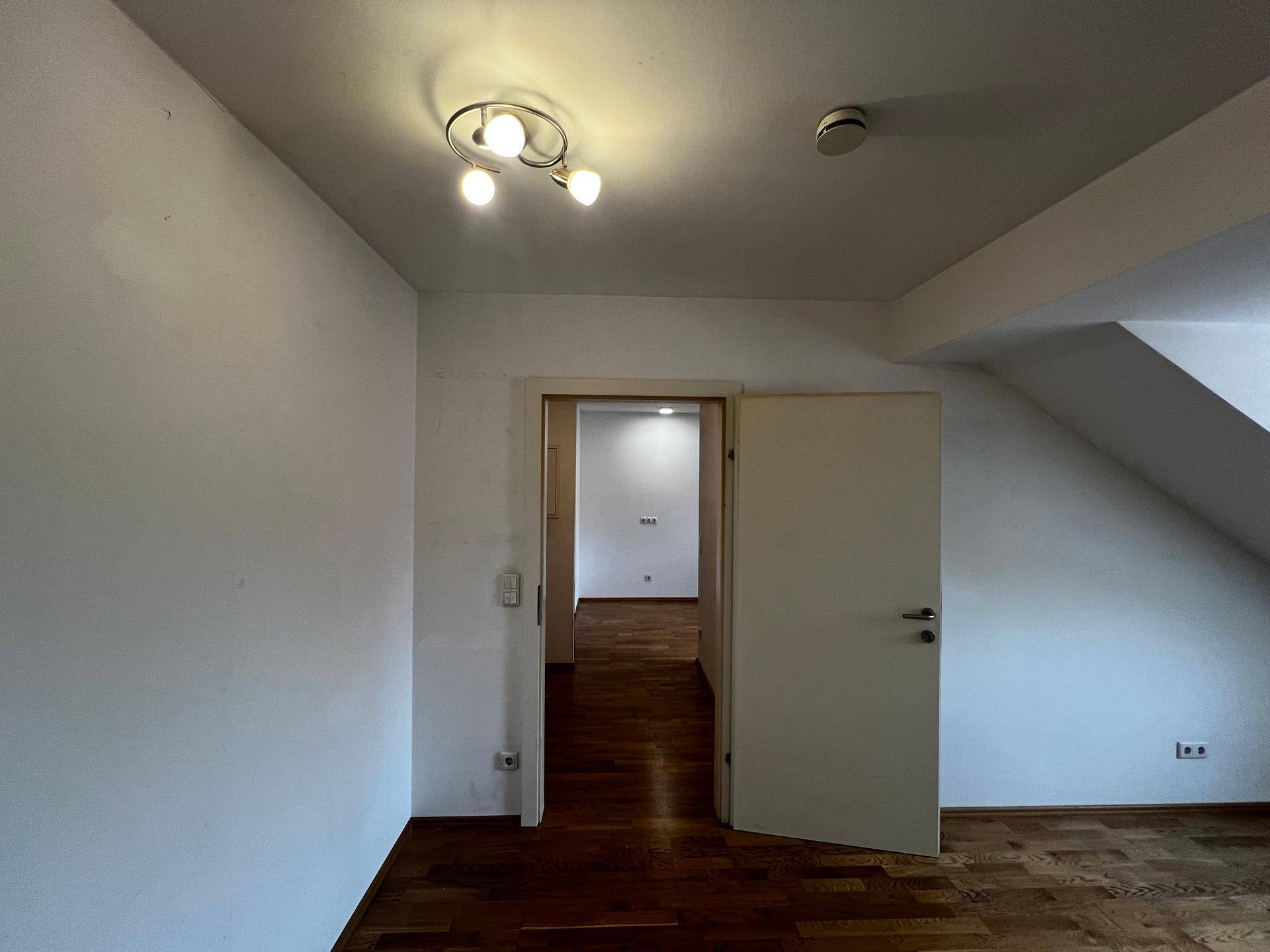 Heller Flur mit Holzboden und einer Deckenleuchte, der zu einem weiteren Raum führt.