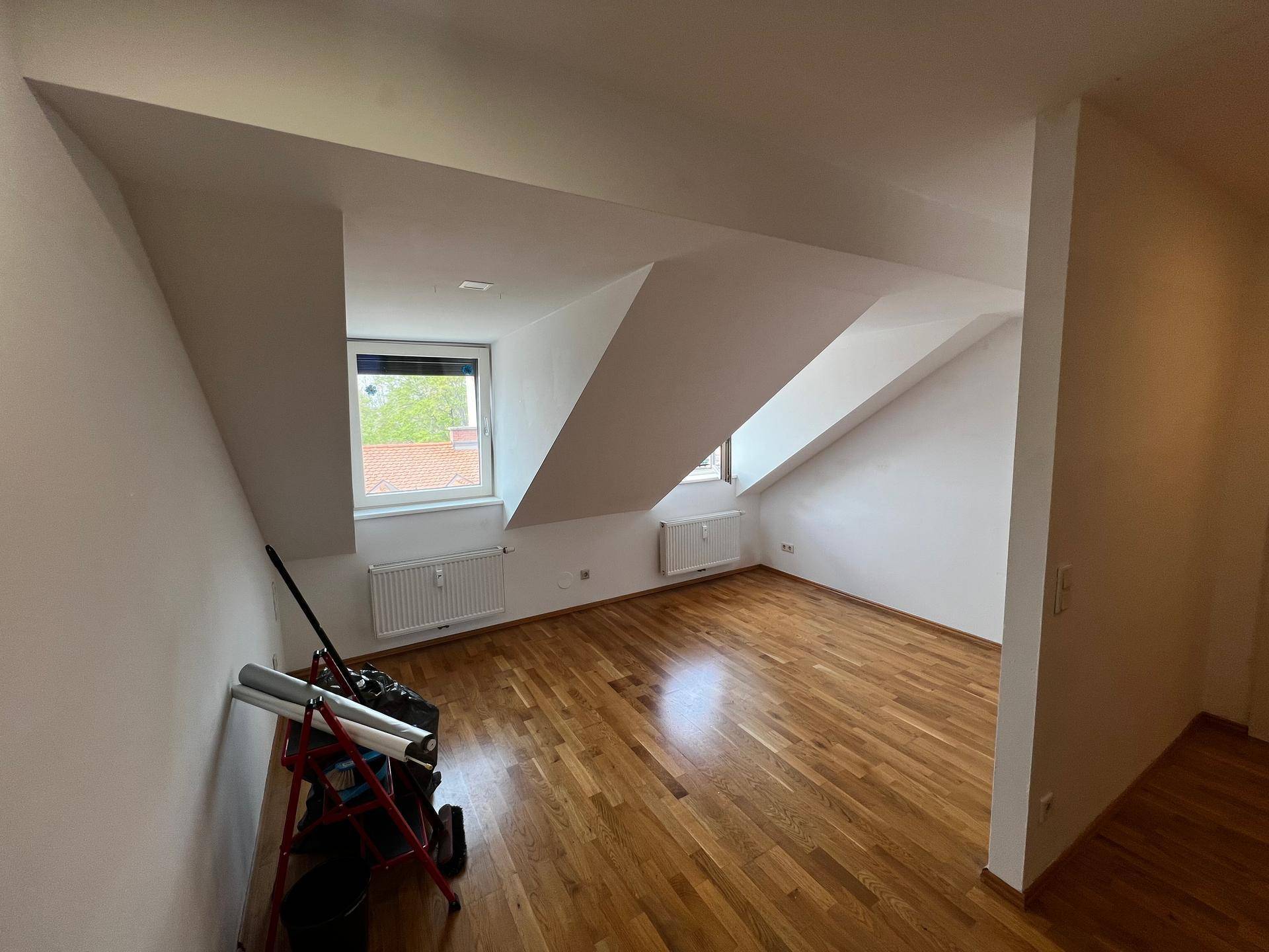 Geräumiger Wohnbereich mit hellem Holzboden, Dachschrägen und Fenstern für natürliches Licht.