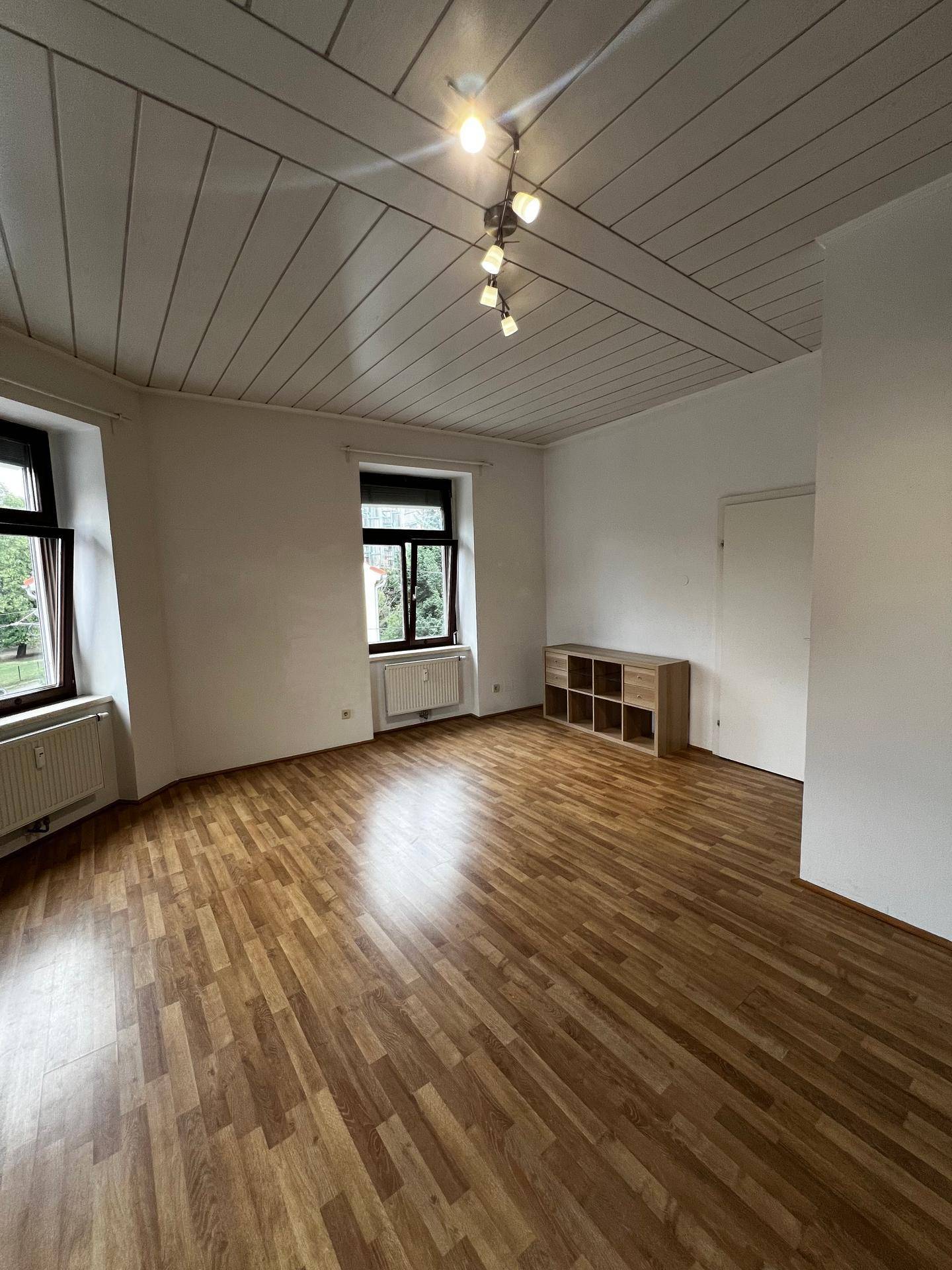 Heller Wohnraum mit Laminatboden, Holzdeckenpaneelen und zwei Fenstern.