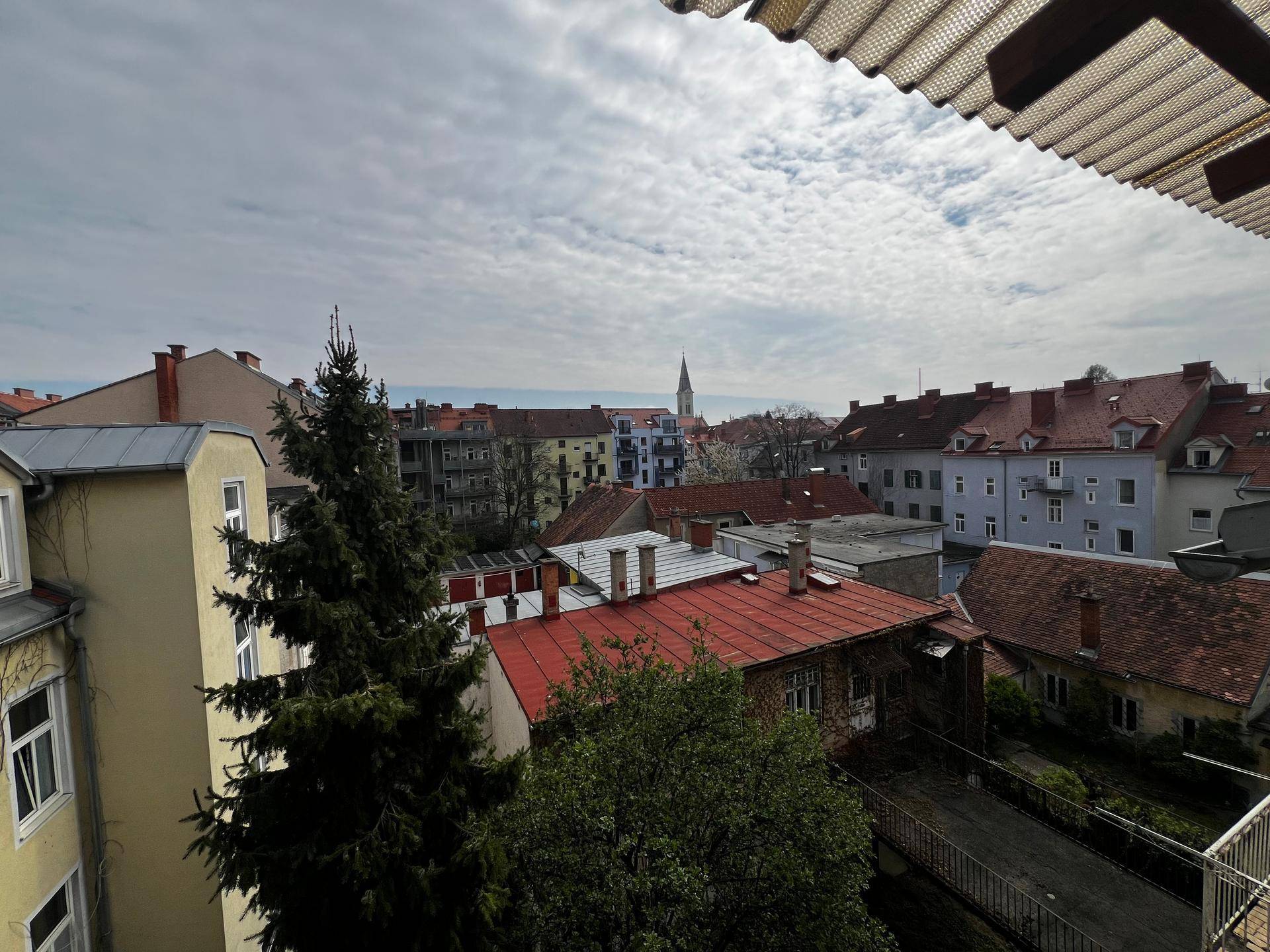 Aussicht vom Balkon über die Dächer der Stadt mit einem Kirchturm in der Ferne.