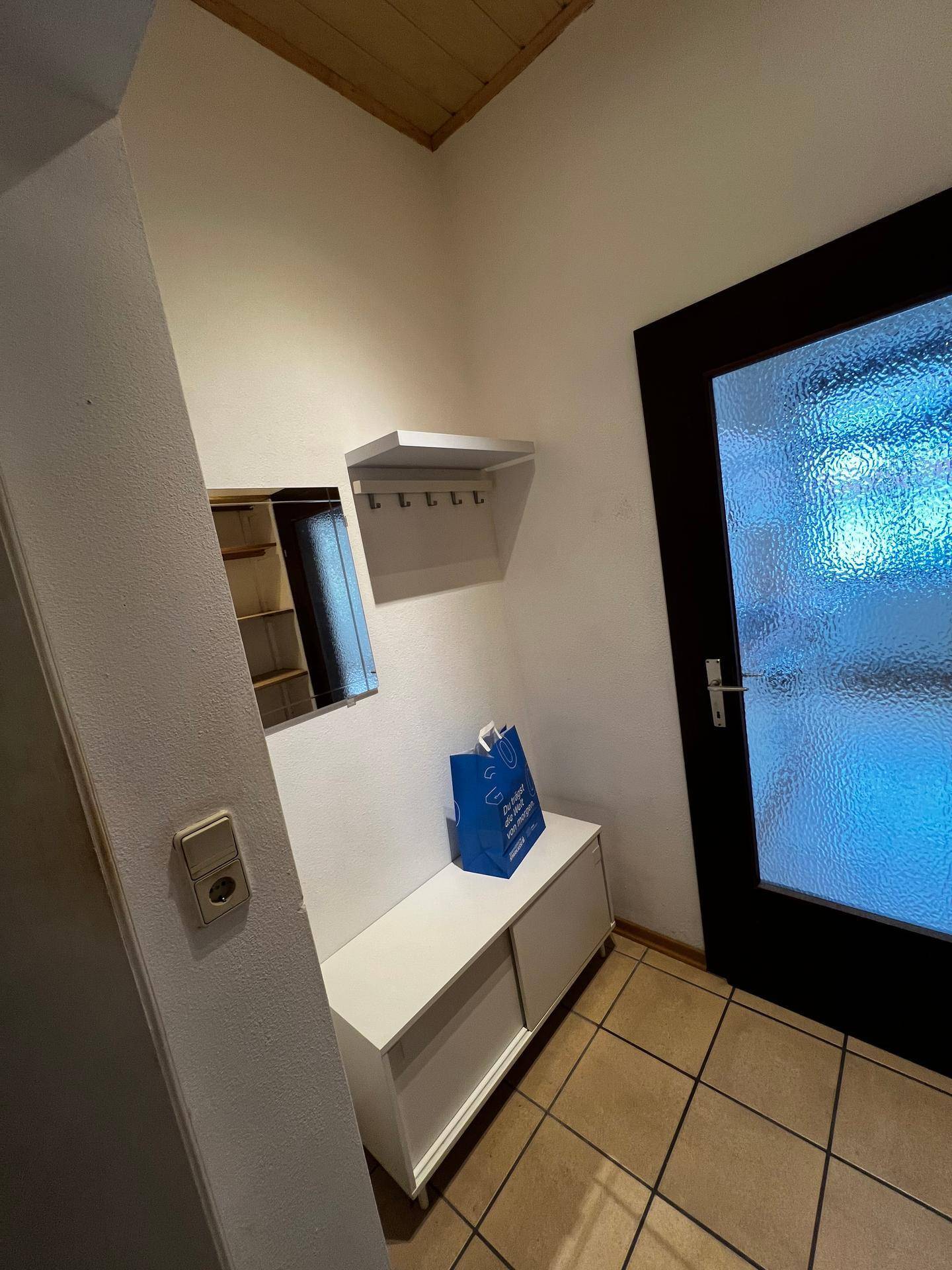 Eingangsbereich mit Fliesenboden, kleiner Garderobe und Spiegel.