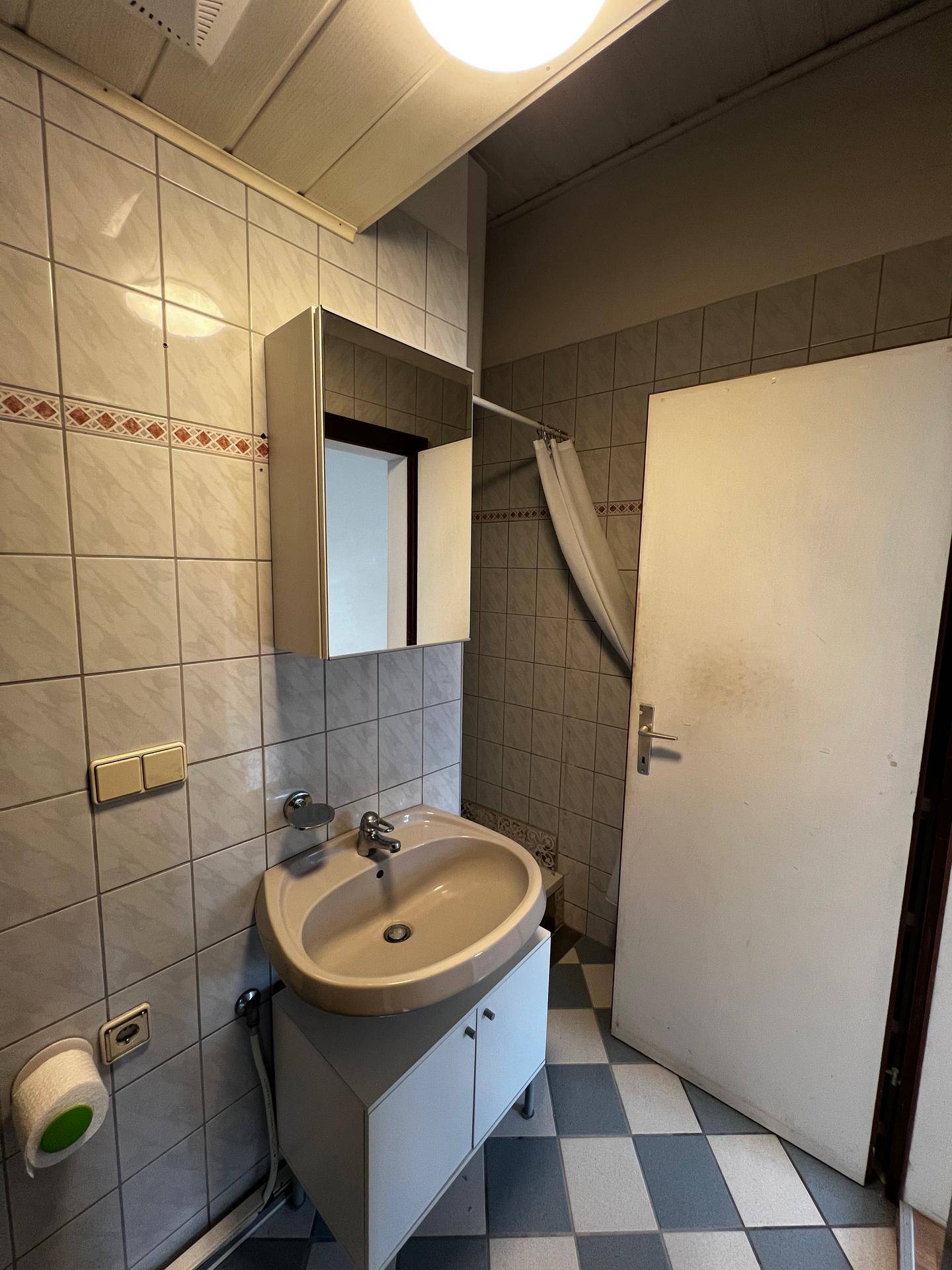 Badezimmer mit beigen Fliesen, Waschbecken und Spiegelschrank, typisch für die 80er Jahre.