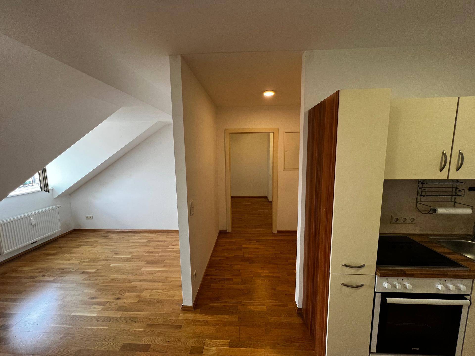 Heller Innenraum mit Holzboden, Dachschrägen und einer kleinen Küchenzeile im Dachgeschoss.