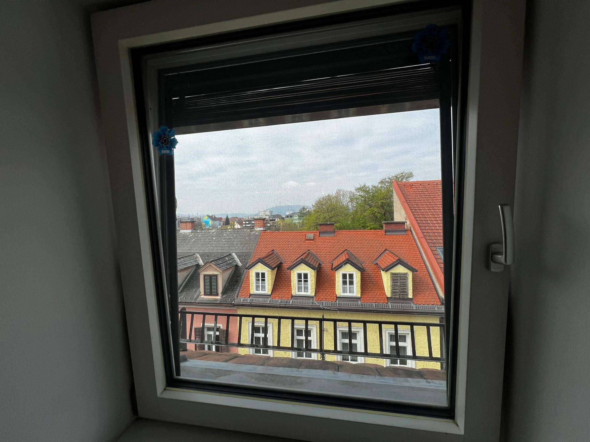 Fenster mit Rollladen und Blick auf die umliegenden Dächer und Gebäude.
