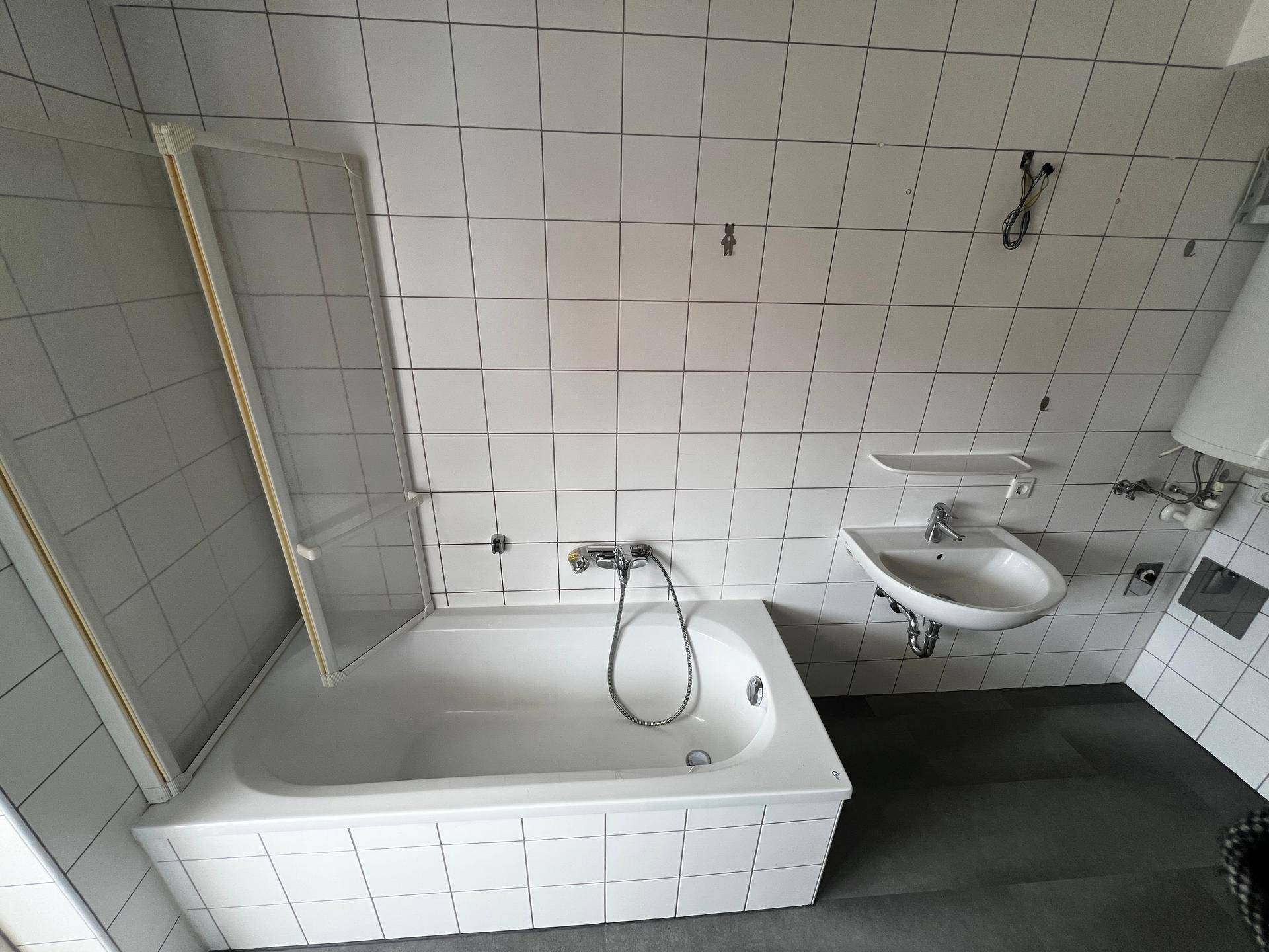 Badezimmer mit Badewanne, Duschabtrennung und Waschbecken, umgeben von weißen Fliesen.