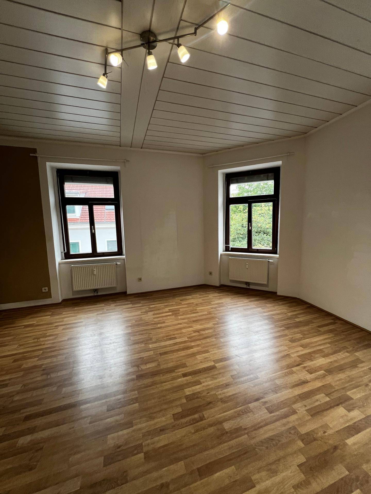 Heller Wohnbereich mit Laminatboden, weiß gestrichenen Wänden und Blick ins Grüne.