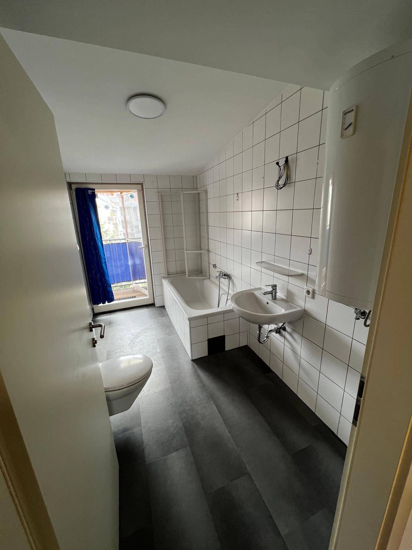 Badezimmer mit weißen Fliesen, Badewanne, Waschbecken und Toilette.