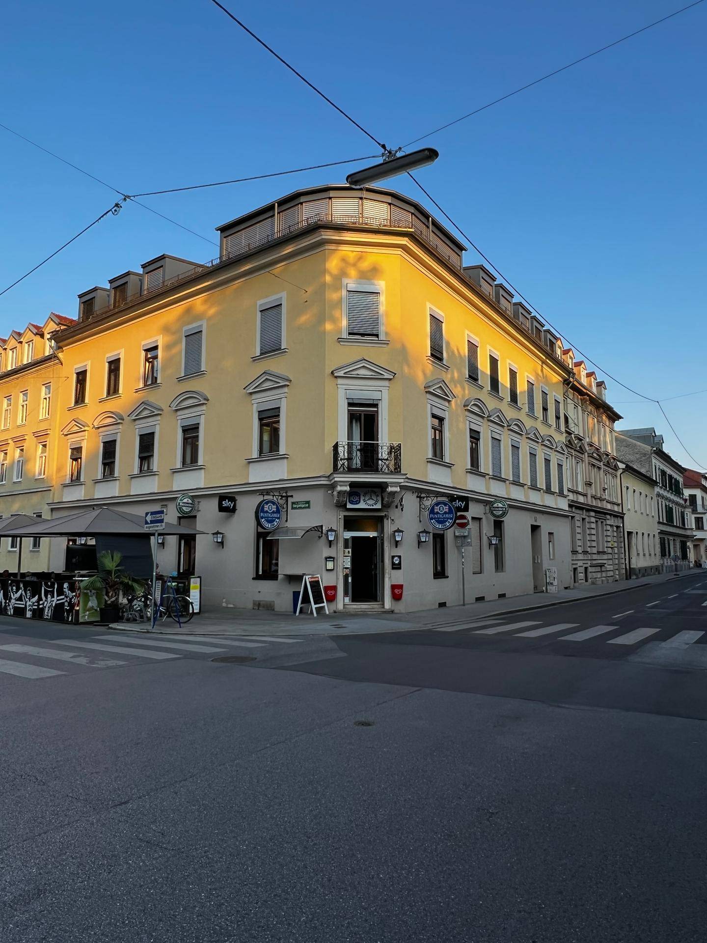 Historisches Eckgebäude mit gelber Fassade und Geschäften im Erdgeschoss bei Sonnenuntergang.