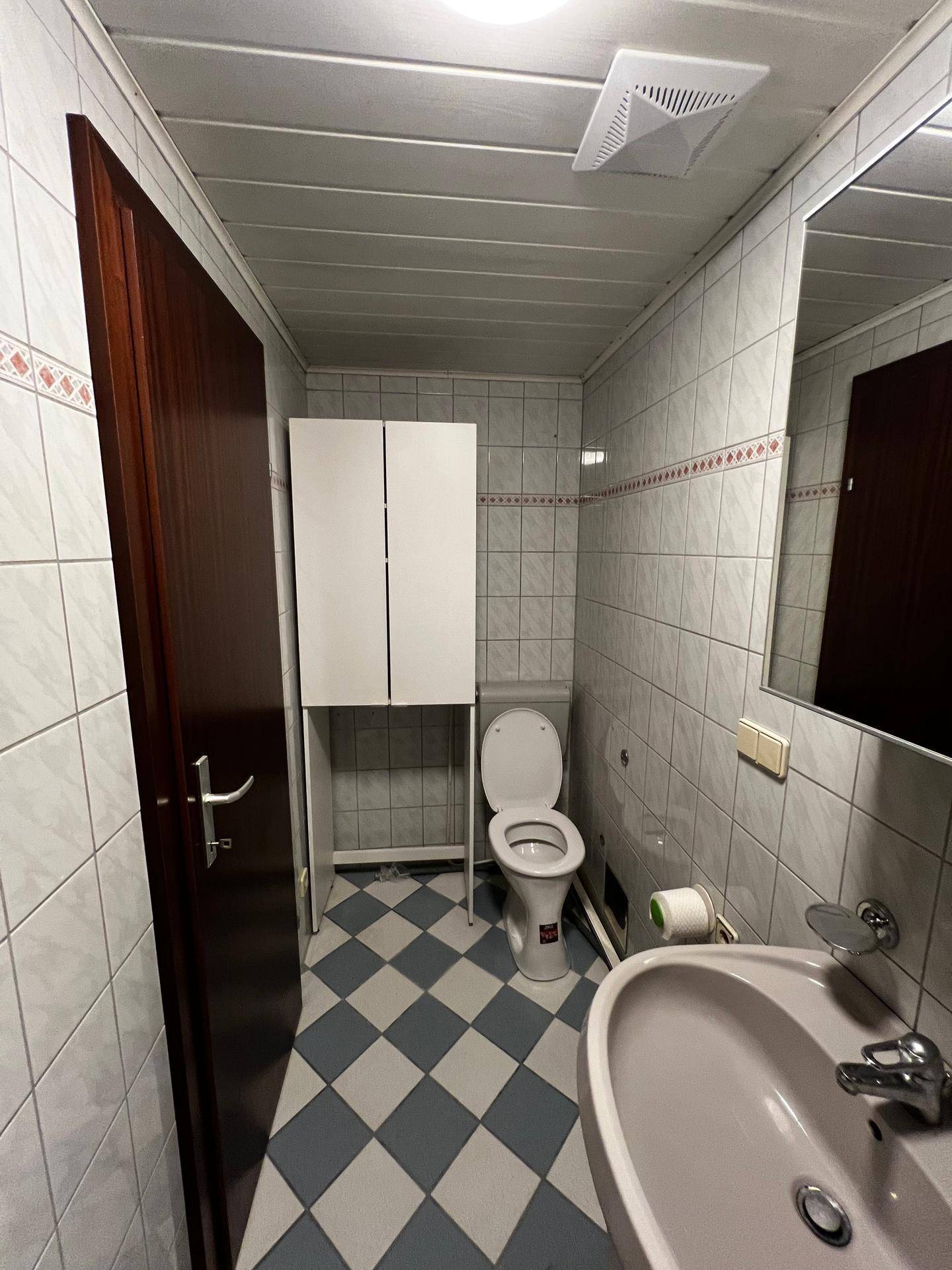 Gefliestes Badezimmer mit Toilette, Waschbecken und Spiegelschrank in älterem Stil.