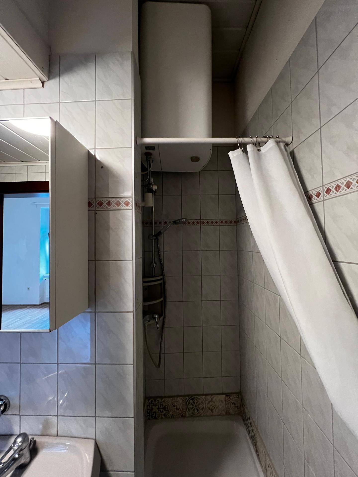 Duschbereich im Badezimmer mit Fliesen, Duschvorhang und Warmwasserboiler.
