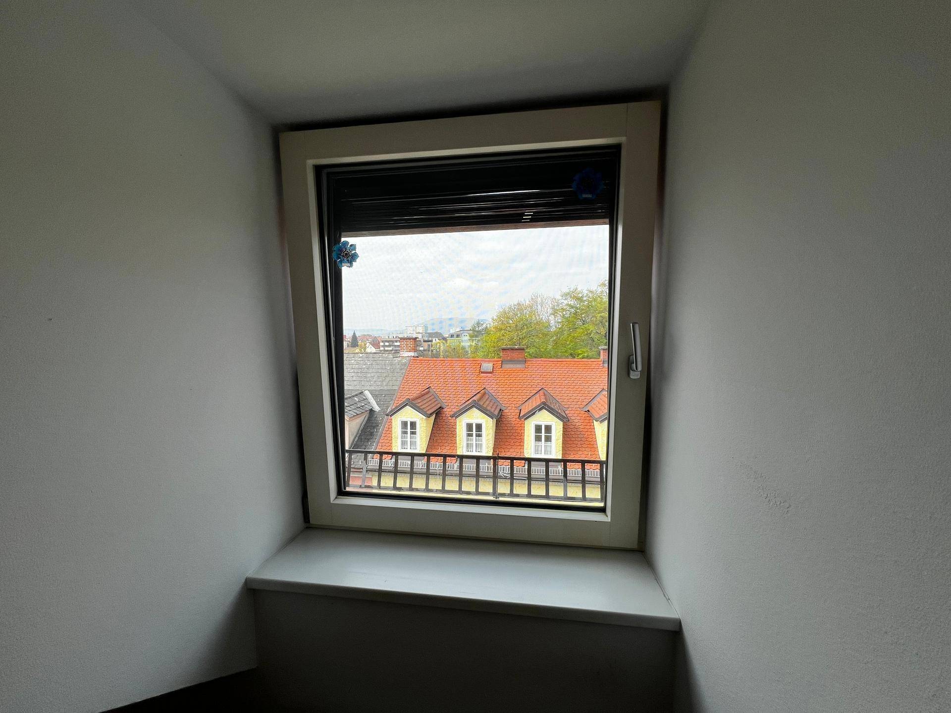 Fenster mit Blick auf die Dächer der Nachbargebäude und den Himmel.