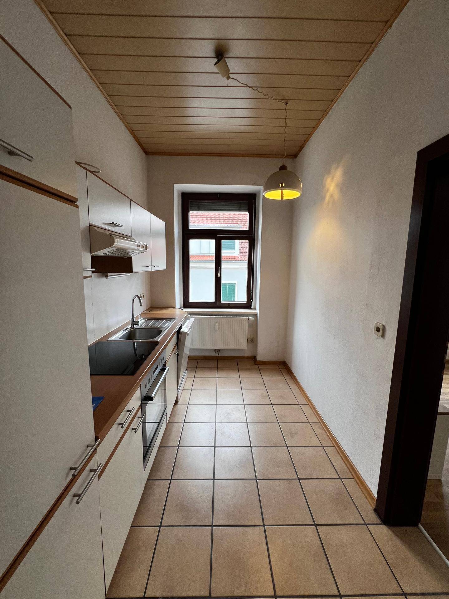 Schmale Küche mit Einbauküche, Fliesenboden und Holzdeckenpaneelen.
