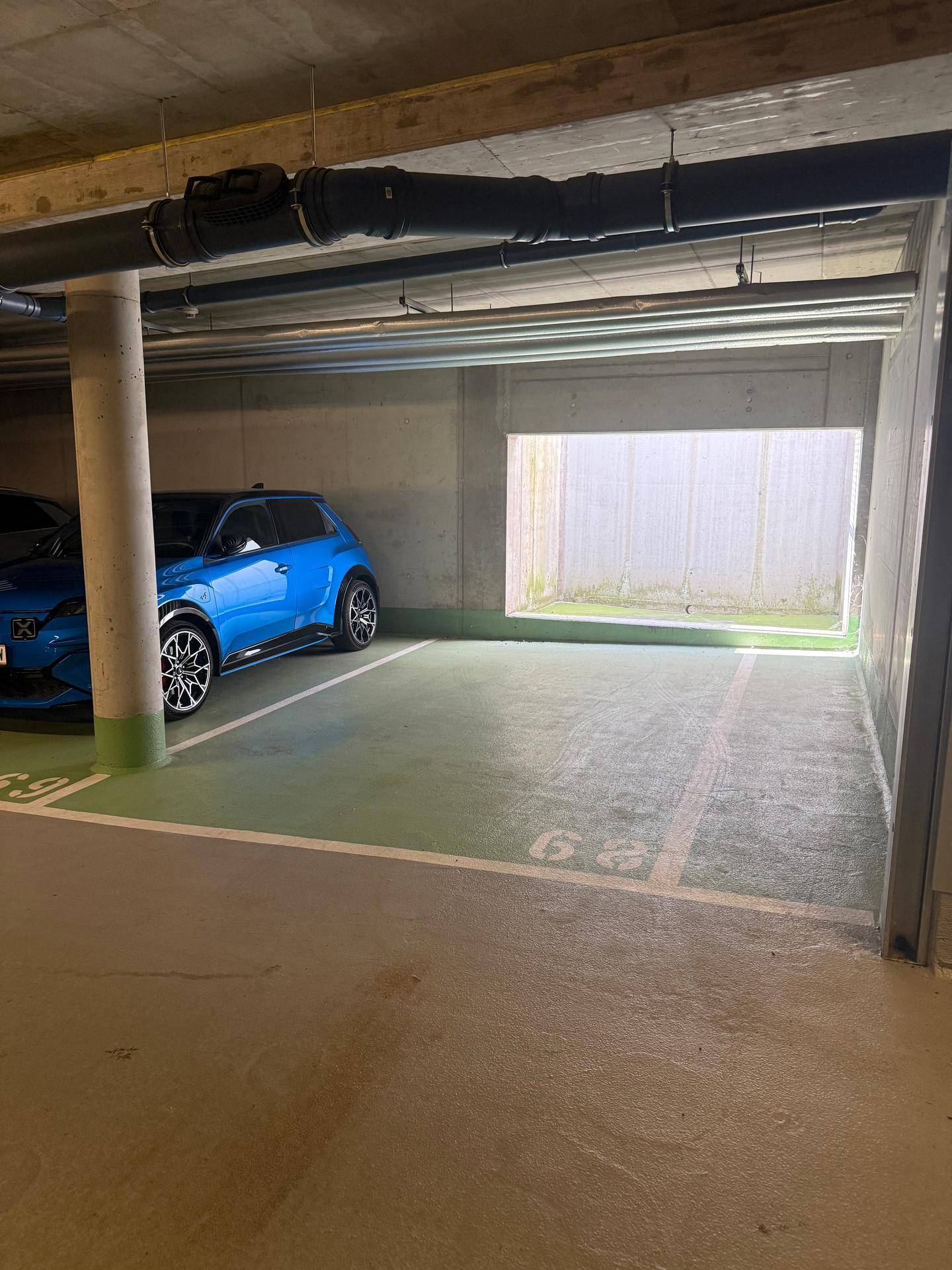 Heller Tiefgaragenstellplatz mit einem blauen Fahrzeug und einer Öffnung für Tageslicht.