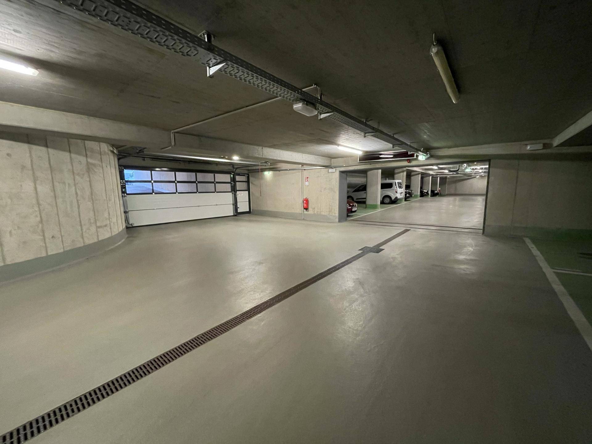 Weitläufige Tiefgarage mit mehreren Stellplätzen, Beleuchtung und einem Garagentor im Hintergrund.